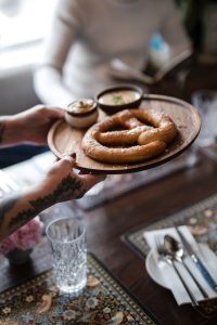 A waitress placing down a plate with a German-style warm pretzil.