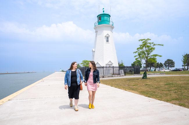Two women walking down the pier with the lighthouse in the background.